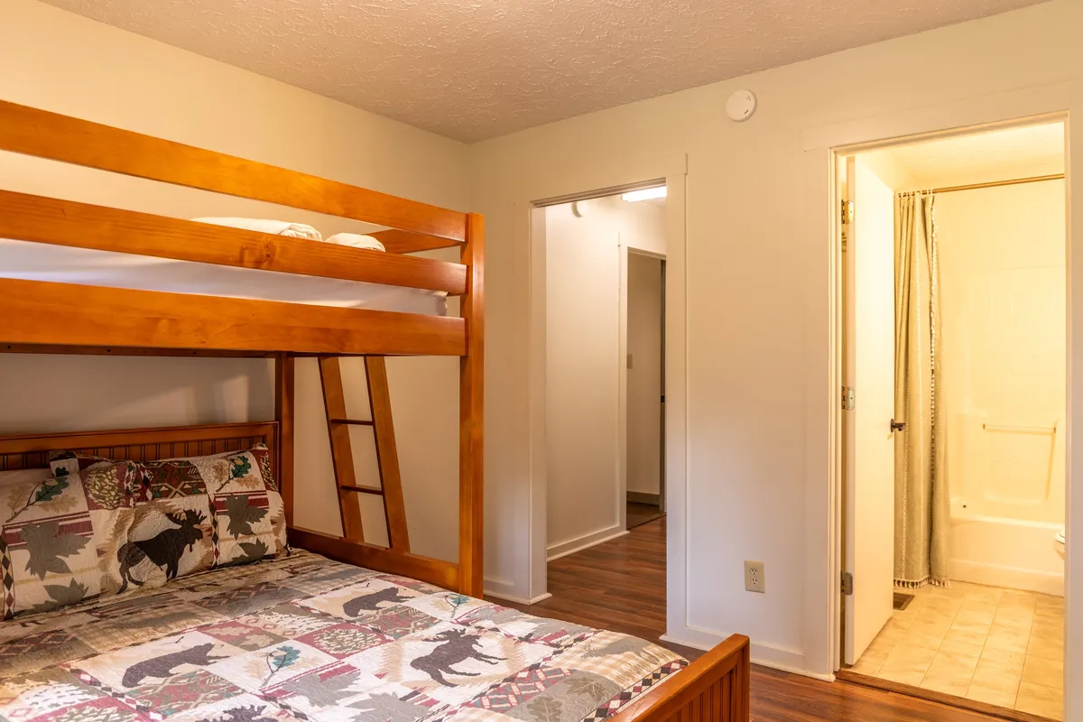 A cozy bunk room with a decorative bunk bed, playful bedding, and a bathroom door nearby. The space invites both relaxation and play, making it perfect for children or singles who love group sleepovers.