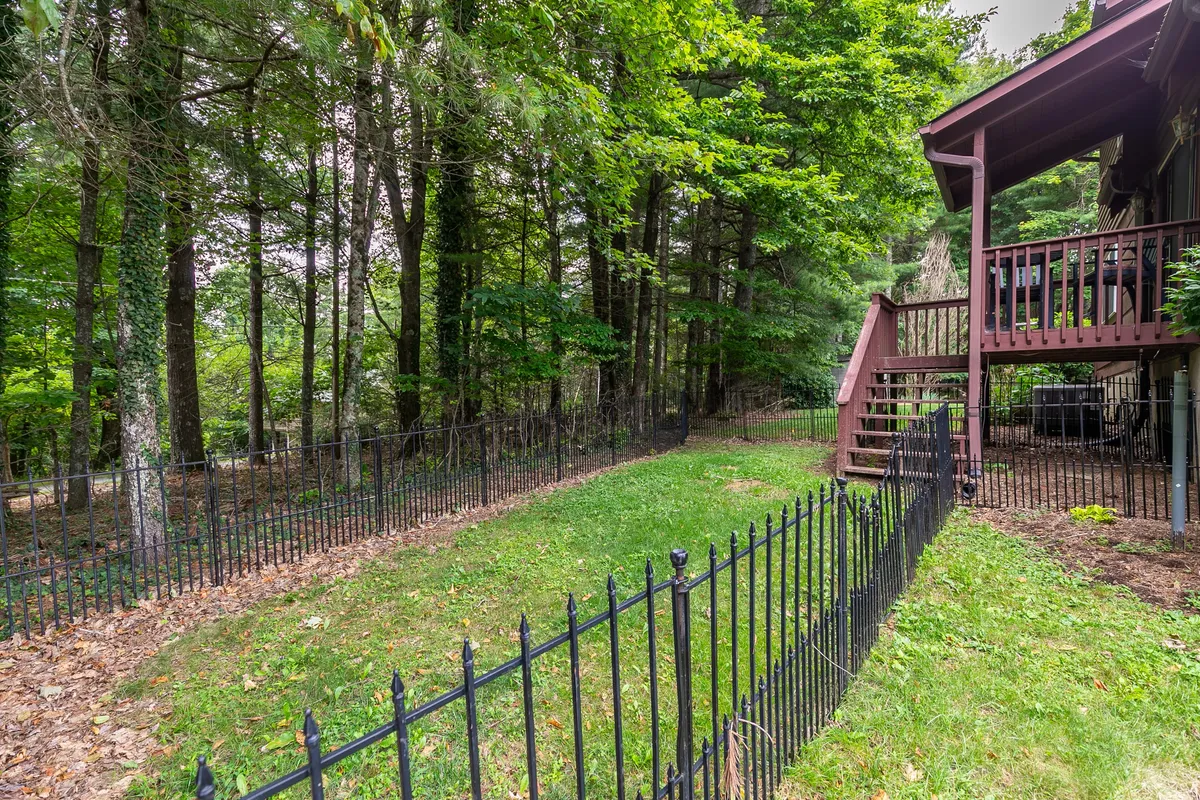 This image features a fenced yard surrounded by trees and the house structure in the background. The open grassy area is perfect for pets to play, while the natural setting reinforces the mountain retreat vibe.