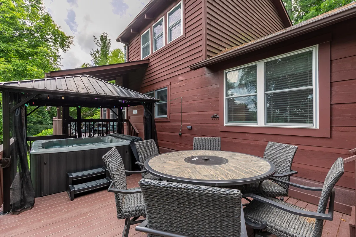 A wooden deck featuring a hot tub, outdoor seating area, and a table set for dining. The space is designed for relaxation and social gatherings, with views of the surrounding nature, hinting at both comfort and the outdoors.