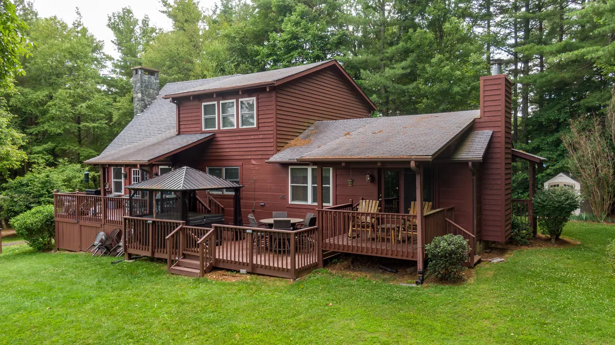 This image captures a spacious wooden deck with an outdoor seating area set against a backdrop of lush trees and a stone chimney. The deck is bathed in warm evening light, inviting families to gather for meals, conversation, or relaxed moments in nature.