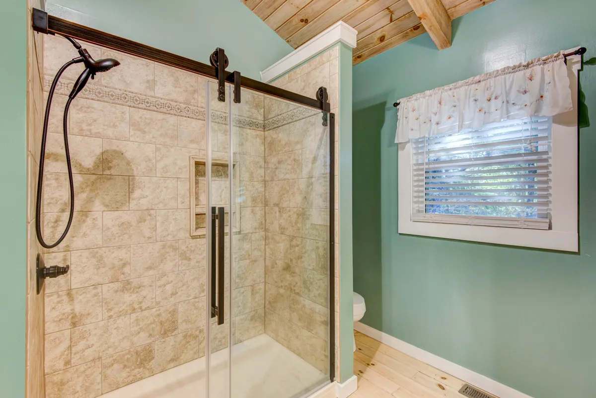 A serene bathroom with a glass shower enclosure, textured tiles, and a wooden ceiling, exuding spa-like calm. The space is inviting and modern, perfect for refreshing after a day’s adventures.