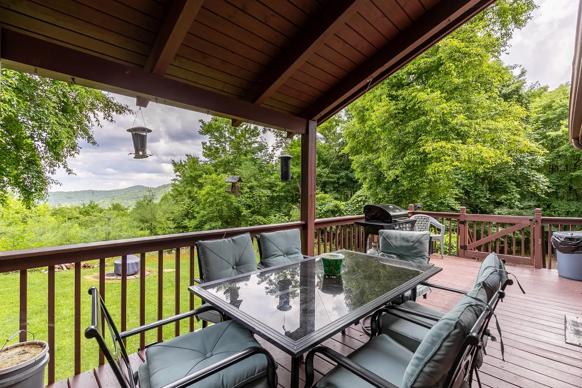 A glass-topped outdoor dining table with comfortable seating is set against a lush, green backdrop with a clear mountain view. The arrangement suggests the perfect spot for alfresco meals, morning coffee, or evening gatherings, all surrounded by nature.