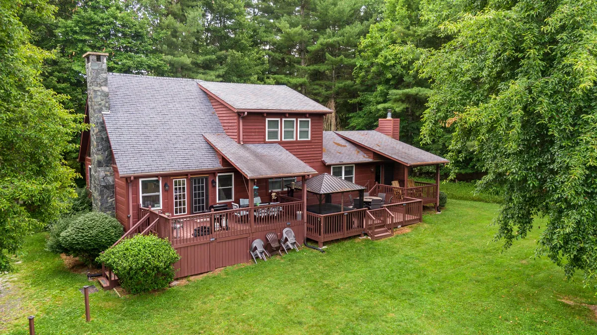 A spacious wooden deck with a stone chimney and comfortable outdoor seating, nestled among lush greenery. The setting is poised for family barbecues, group dining, and cozy evenings by the chimney, all with scenic views.