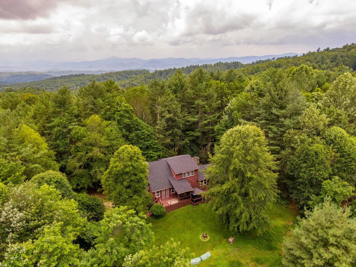 A broad exterior view of the house, framed by surrounding trees and a mountain range in the background. The image conveys peace and seclusion, as well as easy access to outdoor spaces for activities such as hiking, morning coffee, or stargazing.